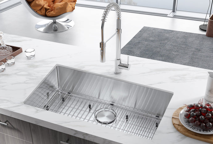 Stainless steel kitchen sink with faucet and accessories on a white countertop.
