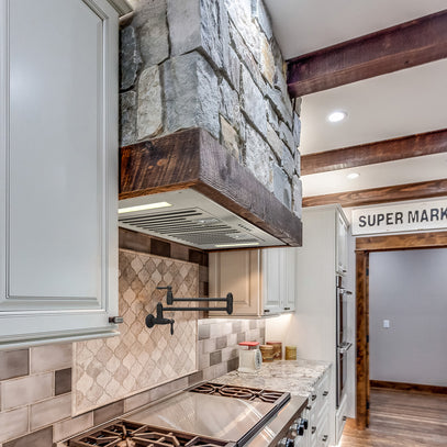 Modern kitchen with stone wall, wooden beams, and stainless steel appliances.
