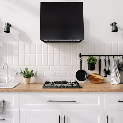 Modern kitchen with black range hood, wooden countertop, and white tiled wall.