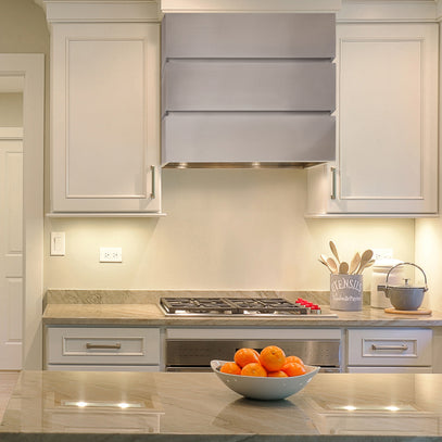 Modern kitchen with stainless steel range hood, stove, and fruit bowl on countertop.
