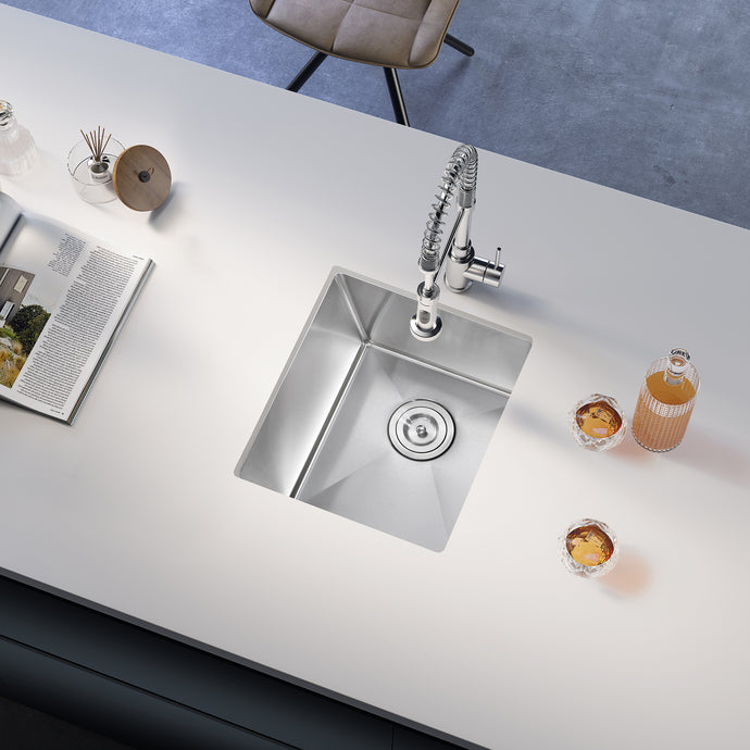 Stainless steel kitchen sink on a white countertop with glasses and a magazine.