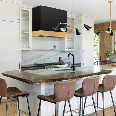 Modern kitchen with wooden island and stools, featuring a black range hood and marble backsplash.
