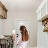 Woman using a smartphone in a laundry room with washing machines and cabinets.