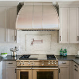 Modern kitchen with stainless steel range and hood, marble backsplash, and dark countertops.