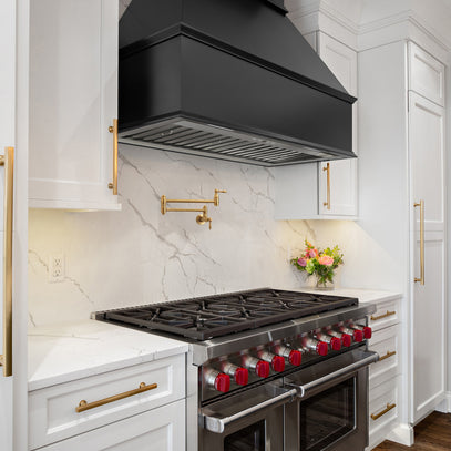 Modern kitchen with a black range hood and stove, white marble backsplash, and gold fixtures.