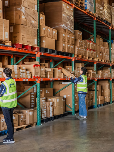 Workers in a warehouse with shelves stocked with boxes